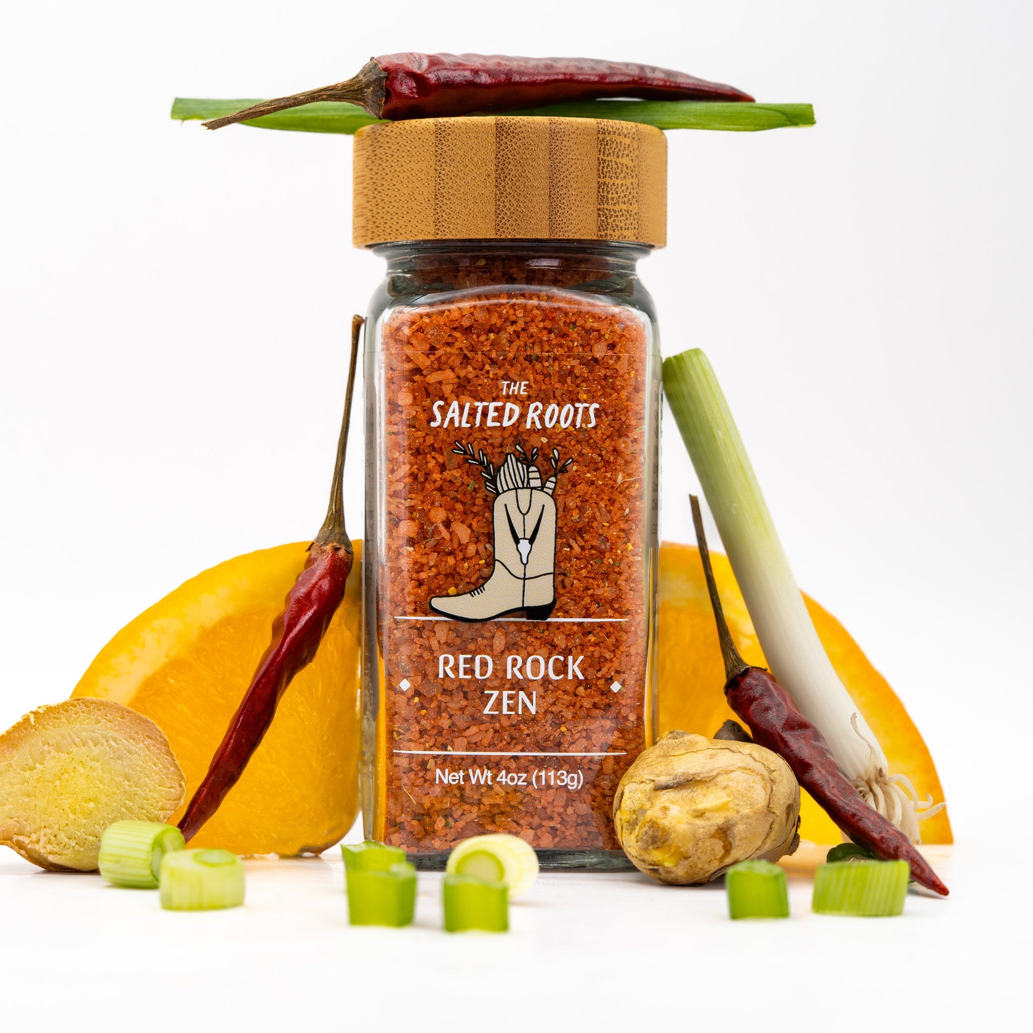 Glass salt jar with wooden lid and labels. Orange, ginger, and scallion slices along with dried pepper sit alongside. 