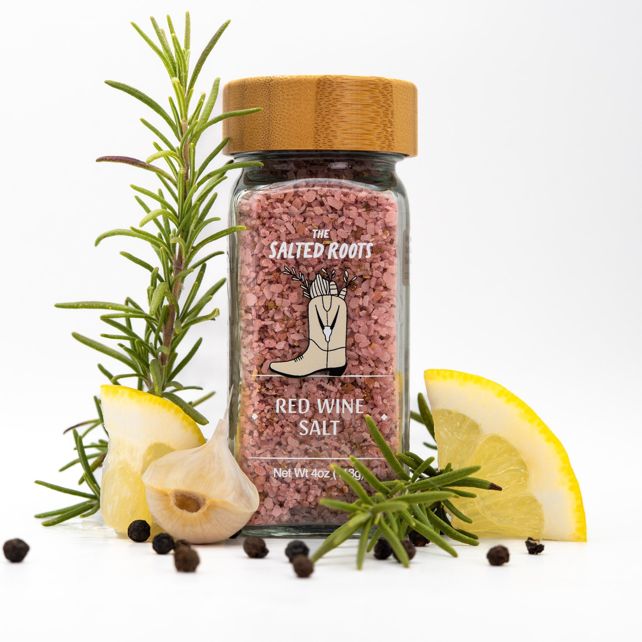 Jar of dark pink salt with wooden lid. Rosemary sprigs, peppercorns, and lemon wedges placed around jar. 