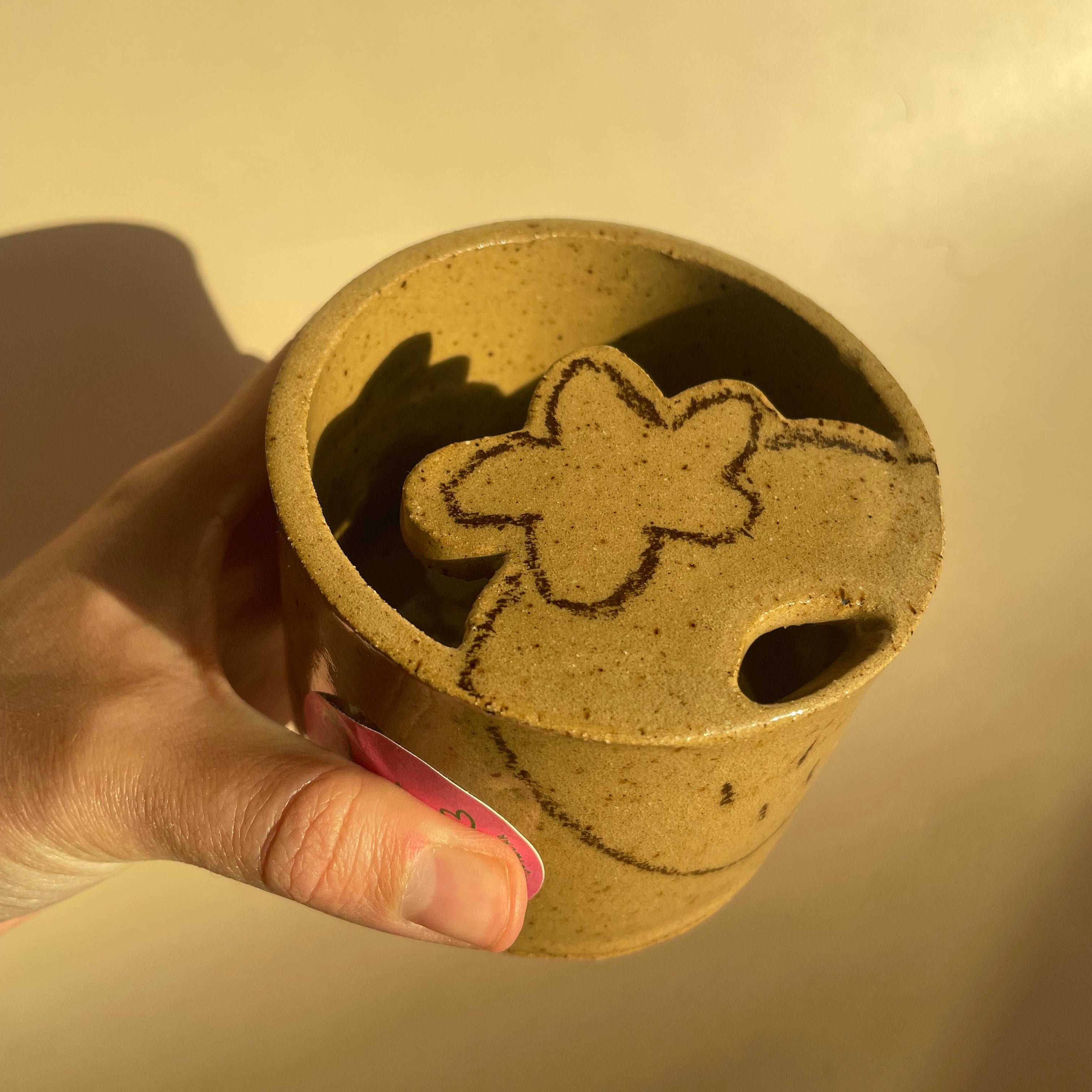 light brown travel mug with lid and sip hole, with dark brown strawberry detail beginning on the lid