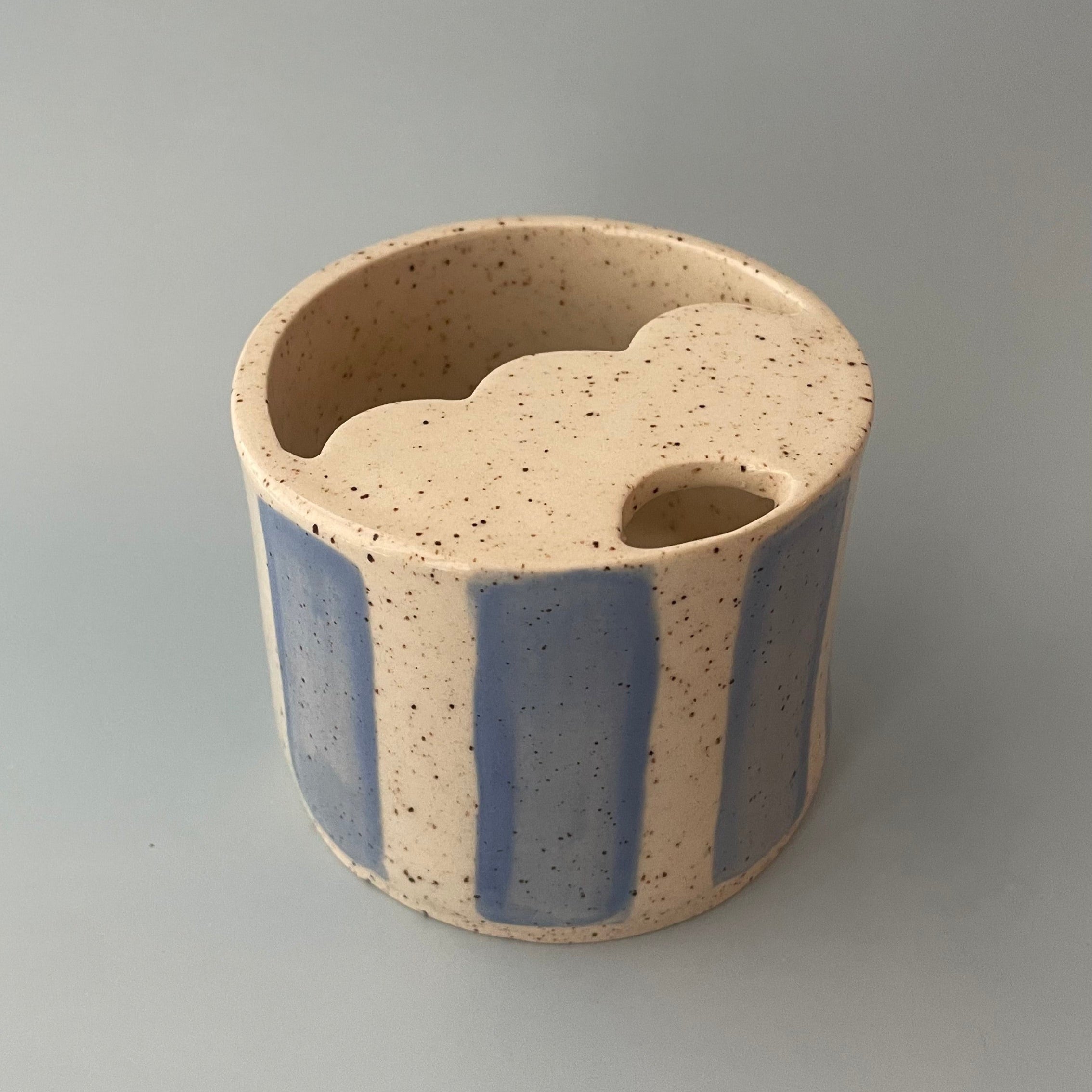 handmade cerqamic travel cup with scalloped lid and a sip hole. finished with an off white base and brown speckles and sky blue stripe details