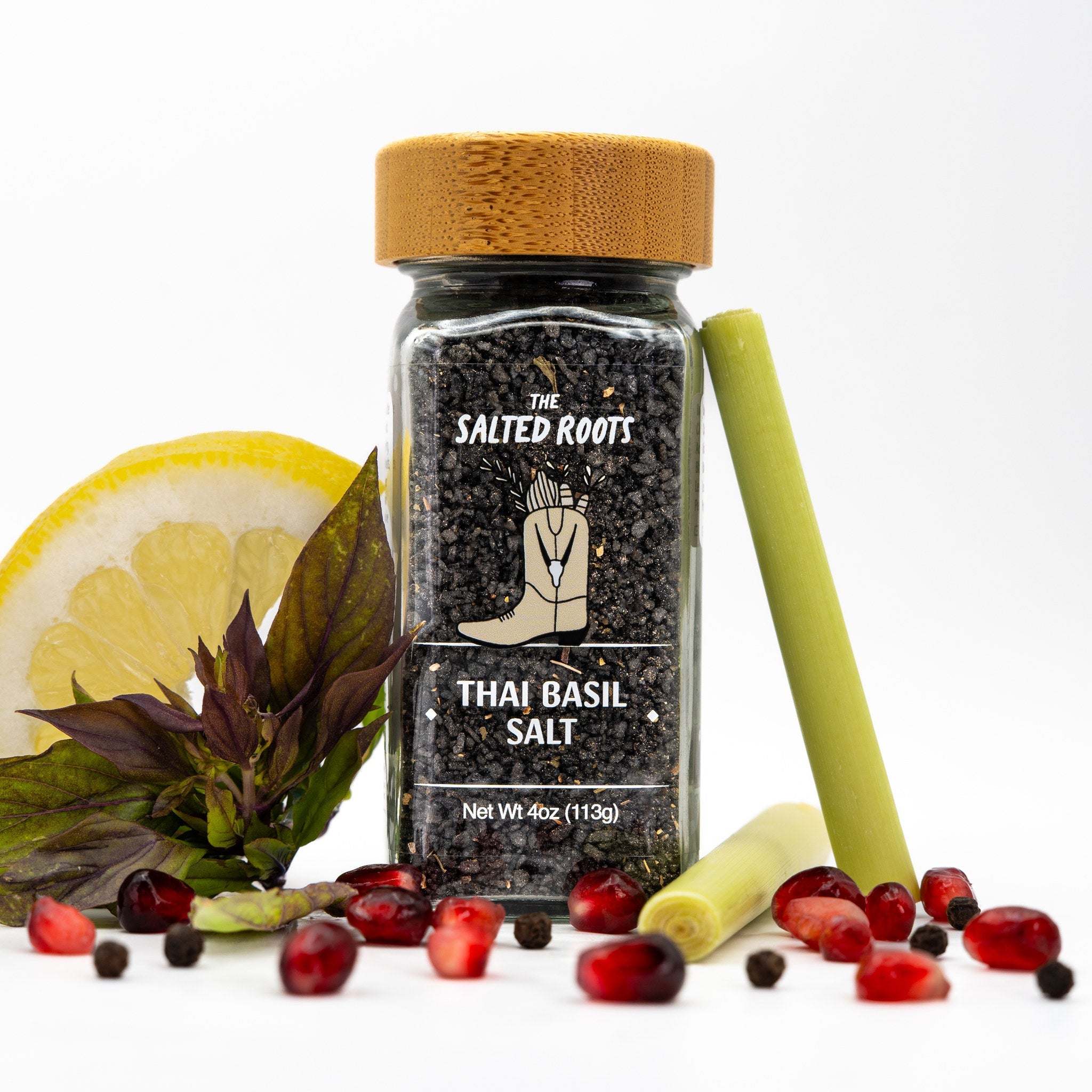Glass salt jar with a wooden lid and label. Lemon wedge, black basil, scallion, and peppercorns scattered around jar. 
