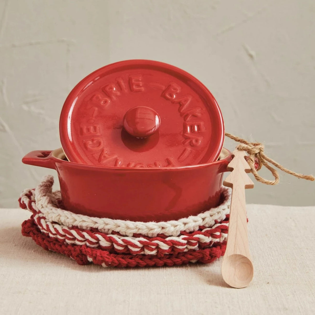 Red enameled cast iron pot with lid, wooden spoon, and red and white woven trivet on a neutral background