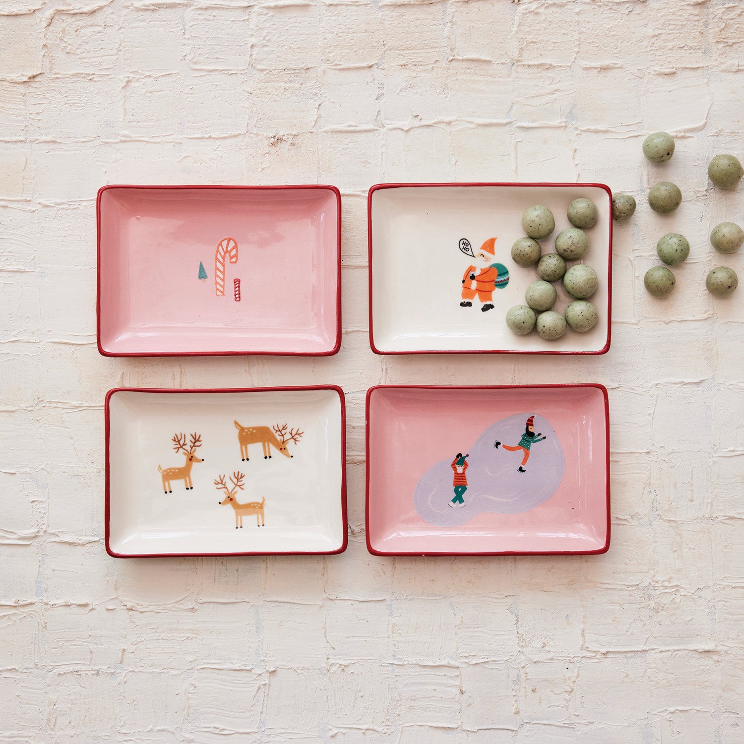 Four pink ceramic trays with Christmas-themed illustrations on a light wooden surface.