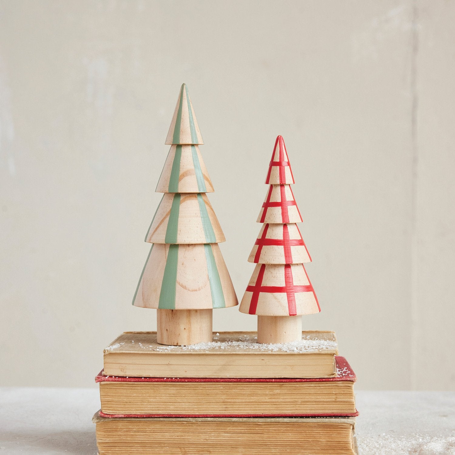 Two wooden Christmas trees on stacked books with a plain background