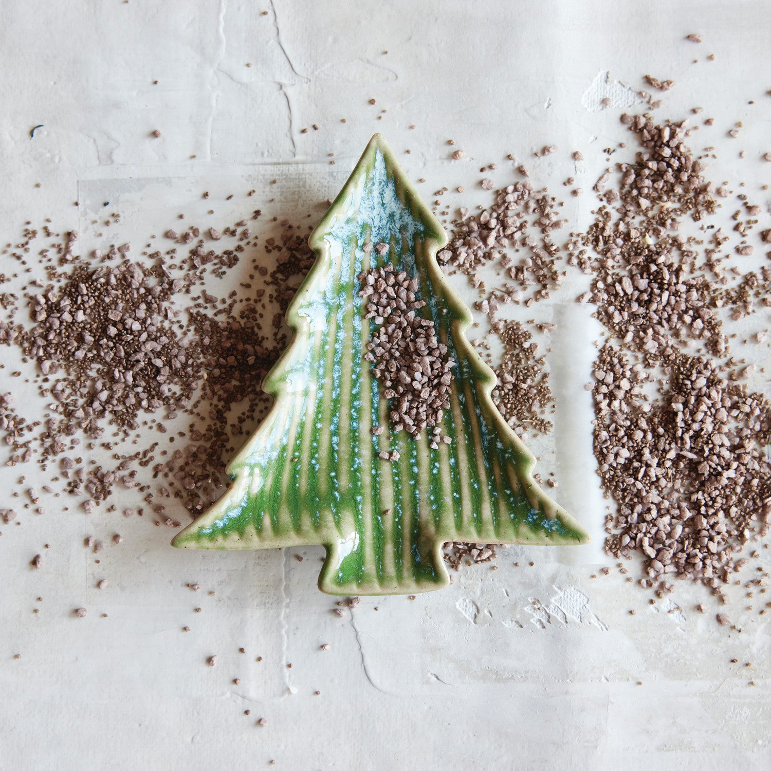 Green ceramic Christmas tree decoration on a textured white surface with brown specks.