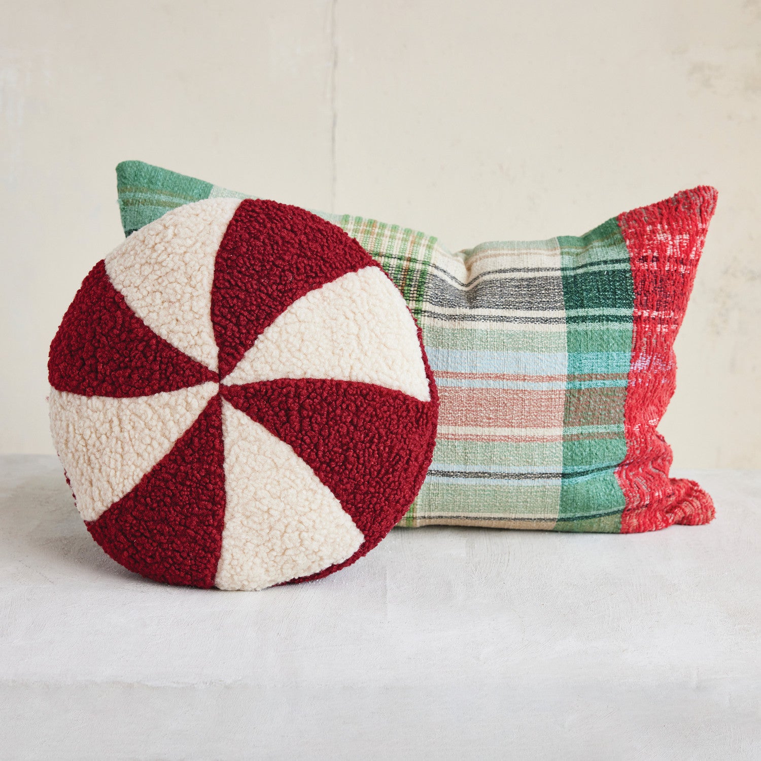 Two decorative pillows, one red and white patterned and the other plaid, on a light background.