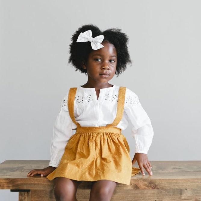 The Andi mini trouser skirt in dark mustard dots has adjustable suspenders with a button on the back. Two button holes are sewn on each suspender strap so your child can grow with their skirt making it easy to wear high on her waist when they are younger & then on their natural waist when older.  This is a shorter skirt that hits above the knee.