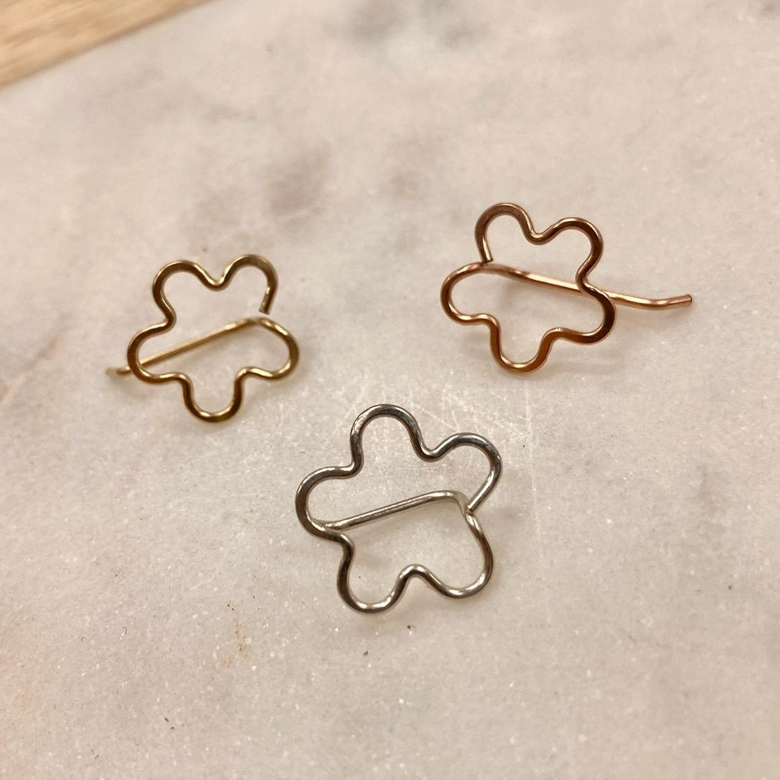 Three flower-shaped bobby pins in gold tone, displayed on a textured surface.