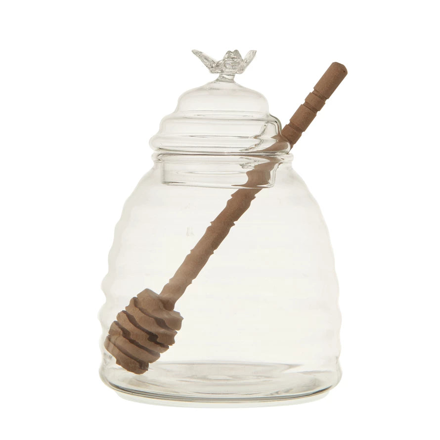 A clear glass honey jar with a bamboo dipper, featuring a lid with a opening for the dipper.